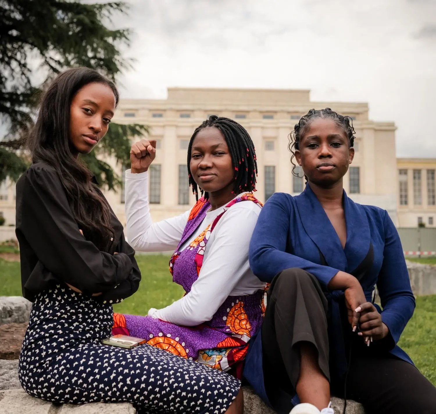 Trois jeunes femmes noires sont assises avec assurance devant un bâtiment des Nations Unies, exprimant leur force, leur unité et leur détermination.